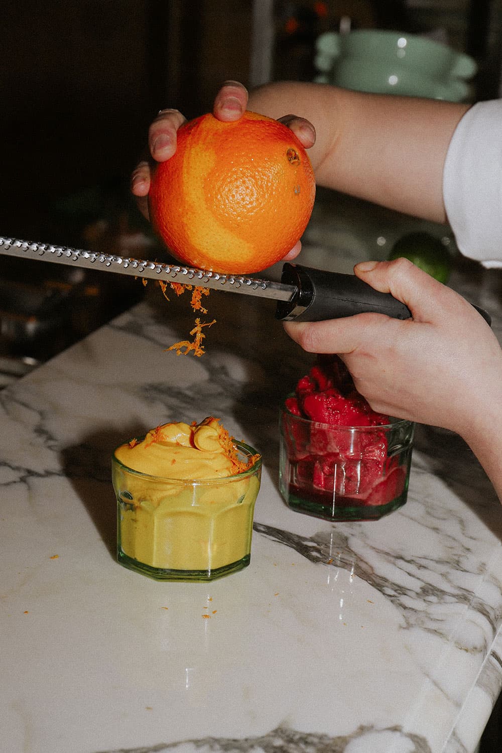 Zest from a grated orange falls onto a fruity cocktail.