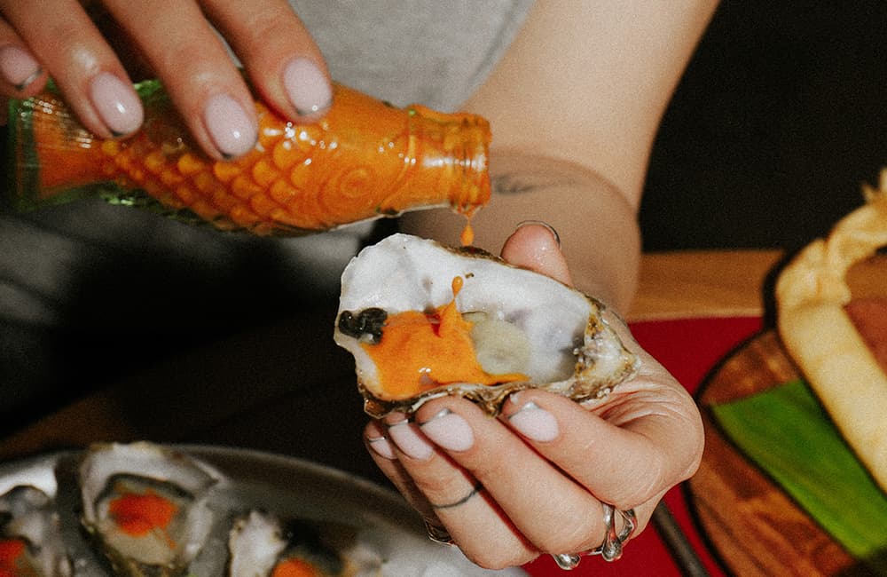 A customer drips hot sauce onto a fresh oyster.