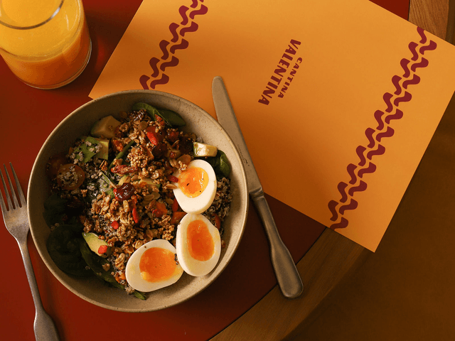 Birds-eye view of a healthy breakfast bowl containing granola and soft-boiled eggs sits on a Cantina Valentina menu.