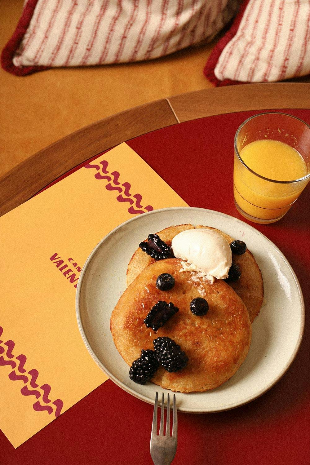 A breakfast of pancakes, blackberries, ice cream and orange juice.