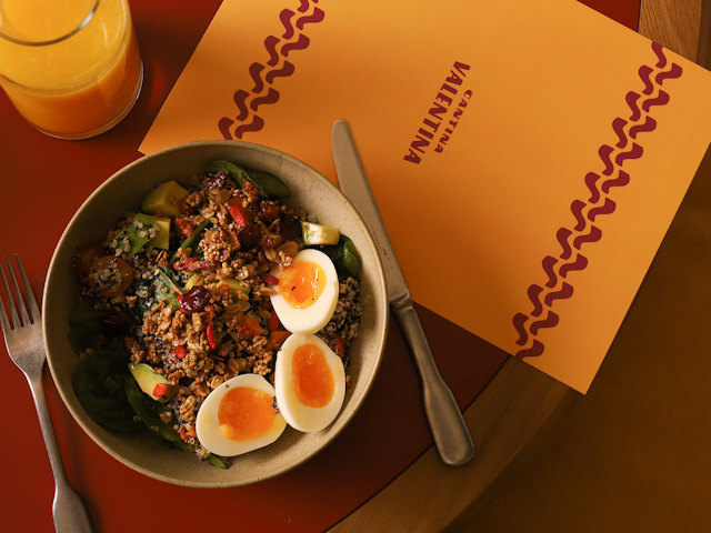 Birds-eye view of a healthy breakfast bowl containing granola and soft-boiled eggs sits on a Cantina Valentina menu.